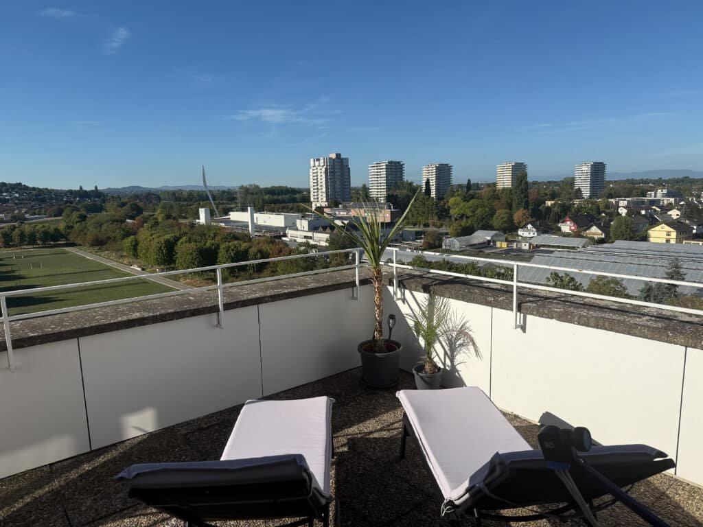 Liegestühle auf der Dachterrasse mit Blick auf Hochhäuser und Grünflächen