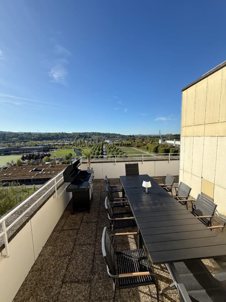 Dachterrasse mit Esstisch und Gasgrill, weiter Blick über Wiesen und Sportanlagen
