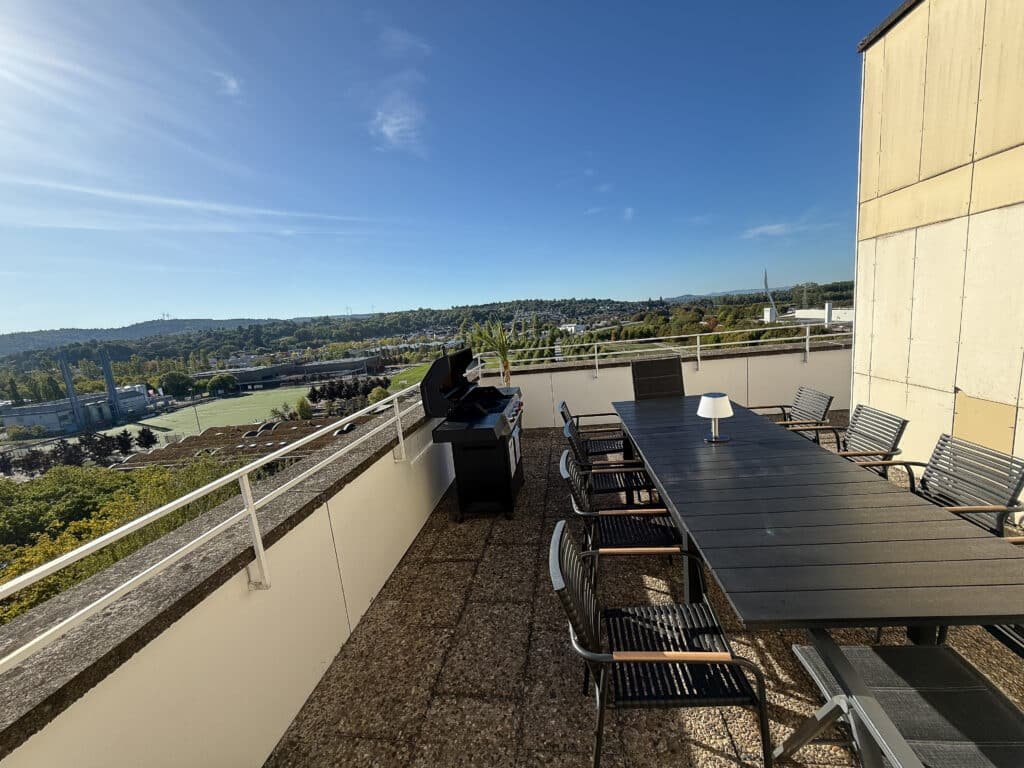 Dachterrasse mit Esstisch und Gasgrill bei strahlendem Sonnenschein